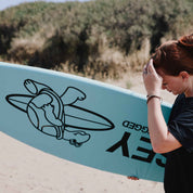 Woman holding a blue surfboard sock with a turtle design on a beach