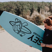 Person holding a blue surfboard sock with a logo and text on a beach