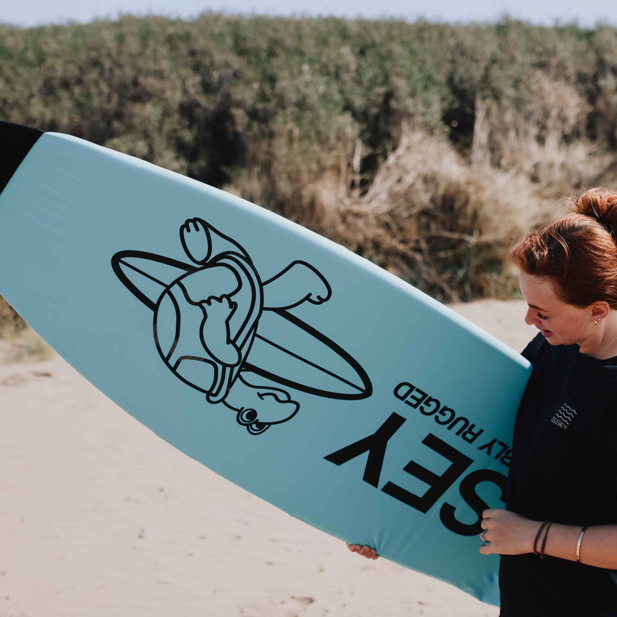 Person holding a blue surfboard sock with a logo and text on a beach