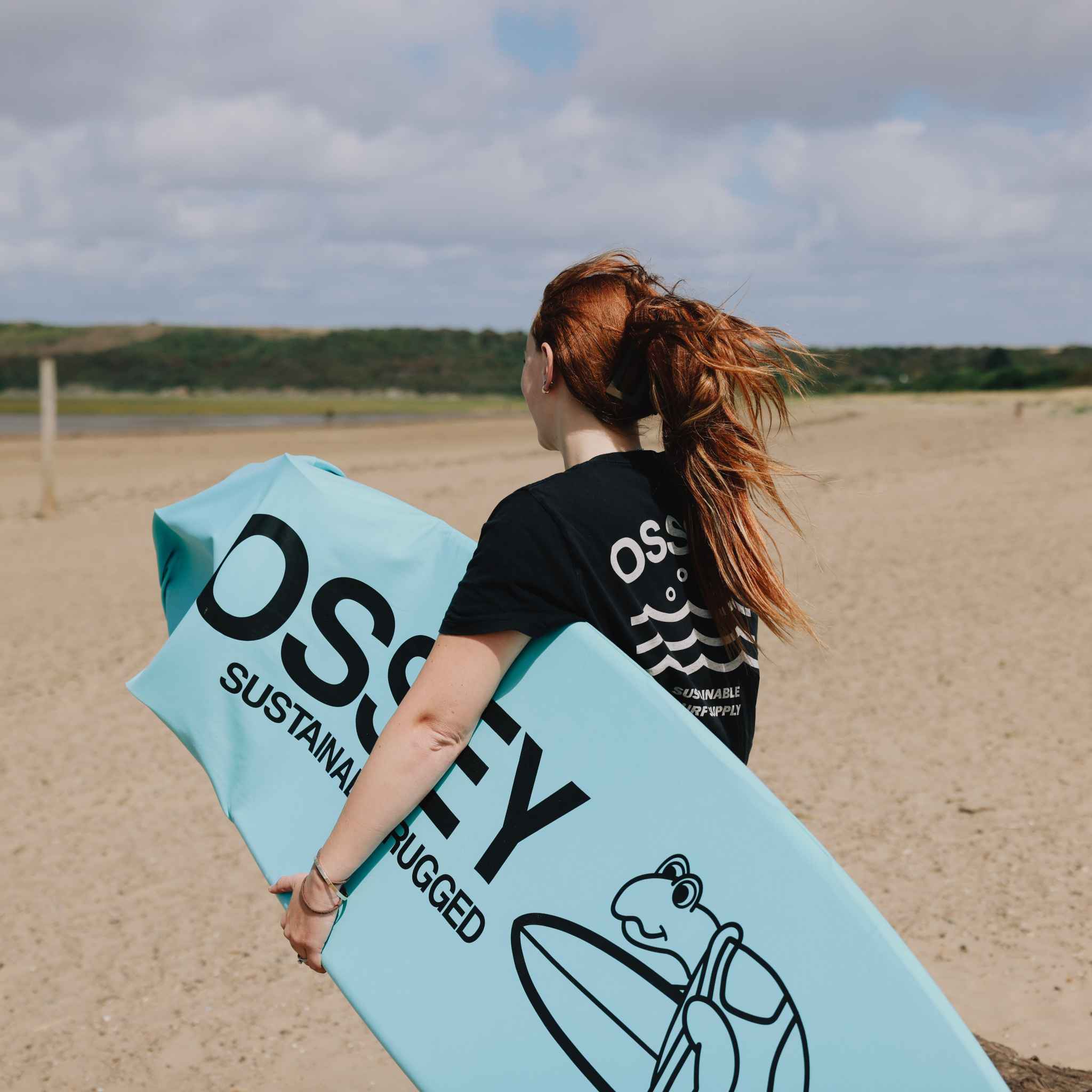 Person holding a blue surfboard sock with branding on a beach